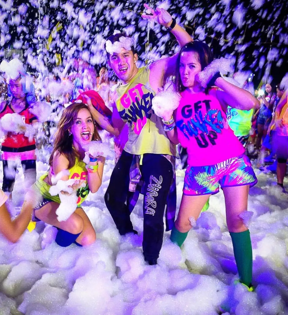 Adults in neon outfits dancing at a glow foam night